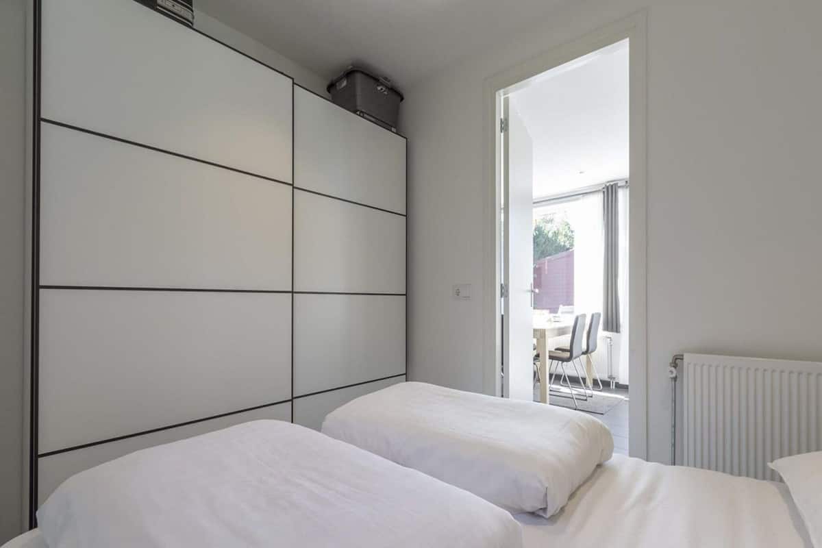 A bedroom with two beds, a large wardrobe, and a view of an outdoor patio area.
