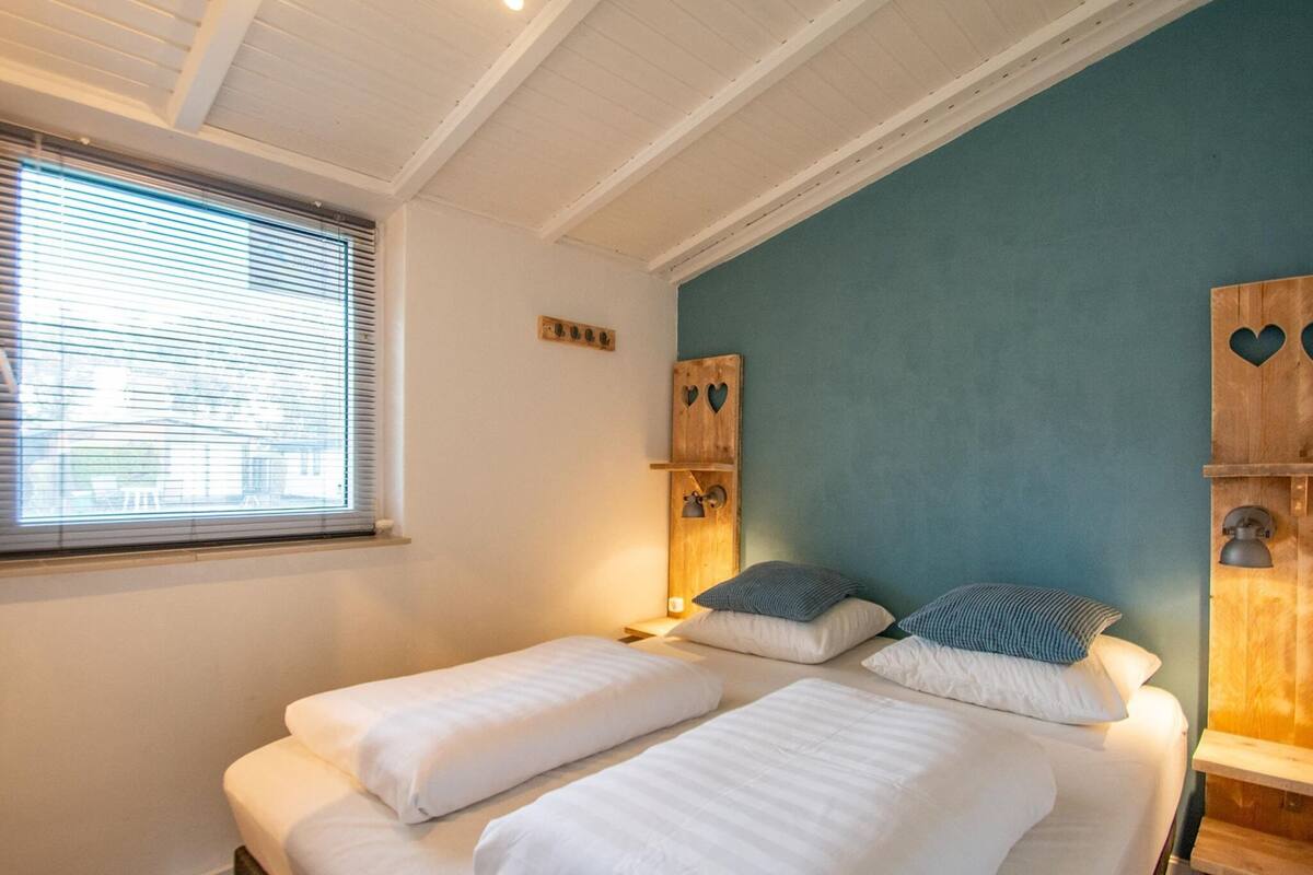 A bedroom with two beds, a window with blinds, and wooden headboards with heart-shaped cutouts.