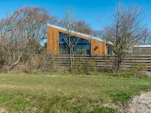 A modern building with large windows and a wooden facade, surrounded by trees and a grassy area.