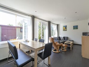 A modern living room with a dining area, large windows, and a view of a building outside.