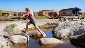 Eine Person überquert einen flachen Wasserlauf mit großen Steinen, umgeben von Gebäuden im modernen Baustil.
