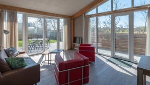 Ein modernes Wohnzimmer mit einem großen Schiebeglasfenster, das auf eine Terrasse führt, einem roten Sofa, einem kleinen Tisch und einer Lampe.