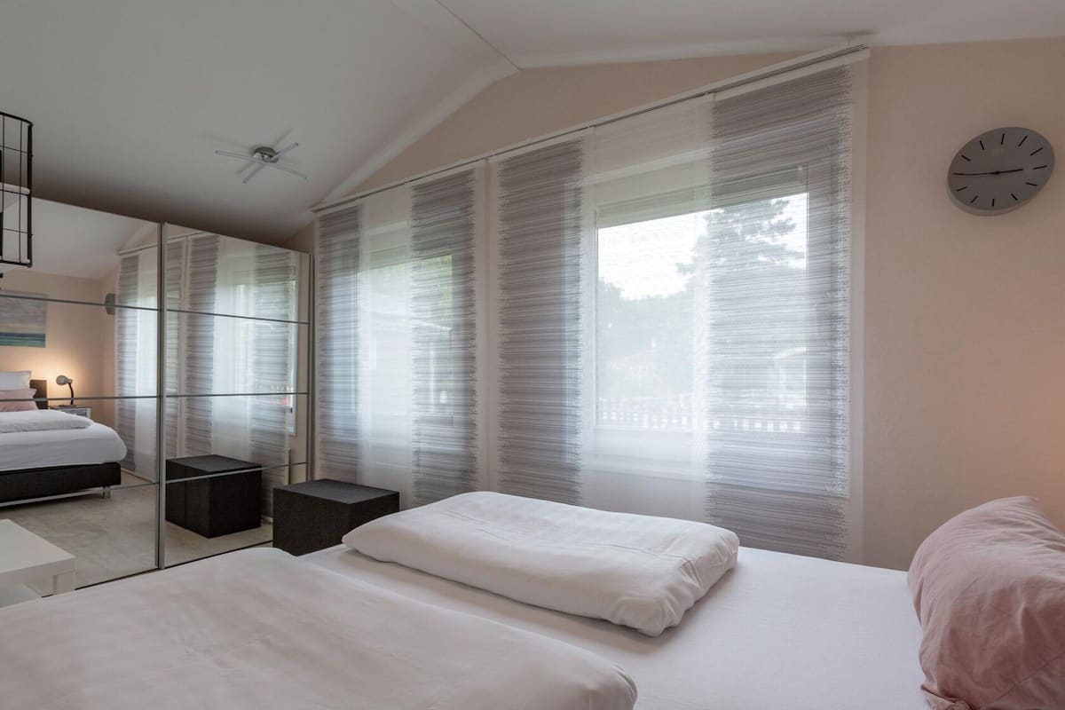 A modern bedroom with a bed, bedside tables, a mirror, and a clock on the wall.
