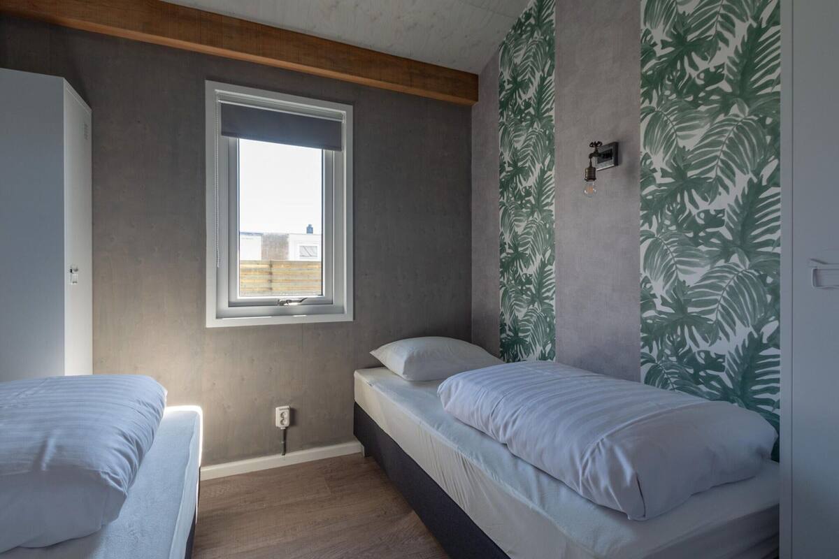 A small, modern bedroom with two single beds, a window, and a wall with a tropical leaf pattern.