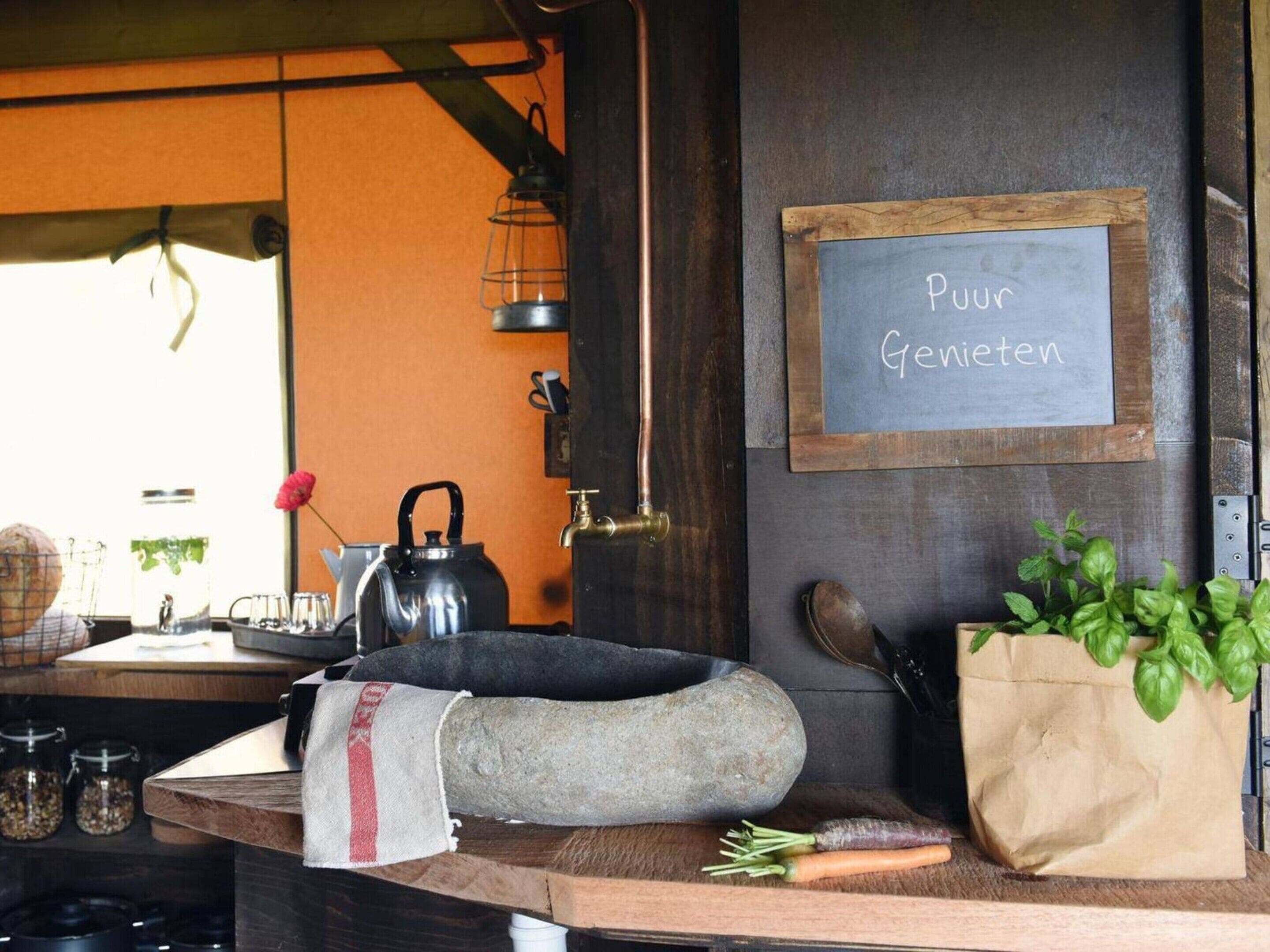 A kitchen counter with a kettle, a stone, a cloth, a bag of basil, and a chalkboard with 'Pour Gemieten' written on it.