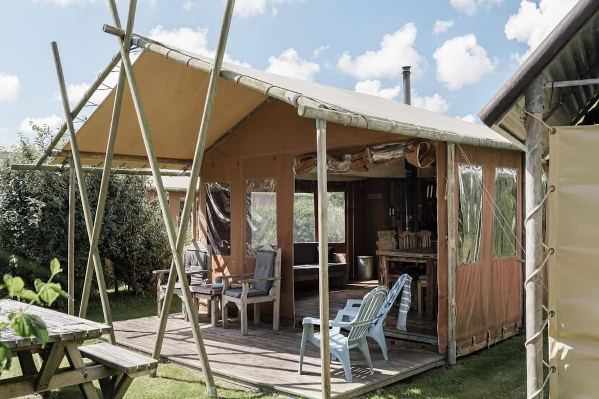 Eine rustikale Holzstruktur mit überdachter Terrasse, Sitzgelegenheiten im Freien und einem einsehbaren Innenbereich mit Esstisch und Stühlen.