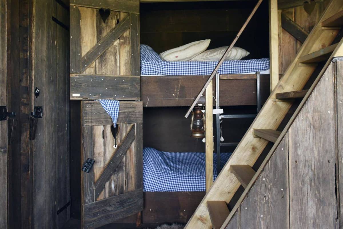 Ein rustikales Holz-Blockhaus-Interieur mit einem Stockbett, einer Leiter und einer Laterne.