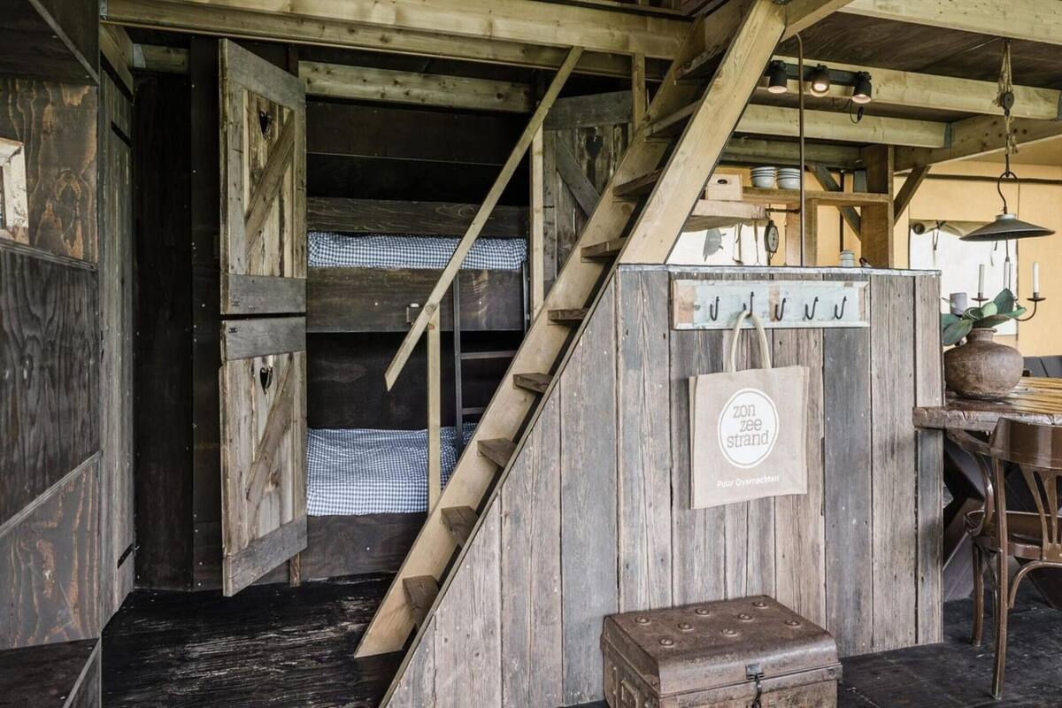 Eine rustikale Holztreppe führt zu einem Schlafniveau mit kariertem Bettzeug.