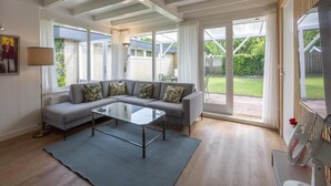 A modern living room with a sectional sofa, a glass coffee table, and large windows offering a view of the backyard. - Comfortable Holiday Home in Sint Maartenszee (Sint Maartensvlotbrug)