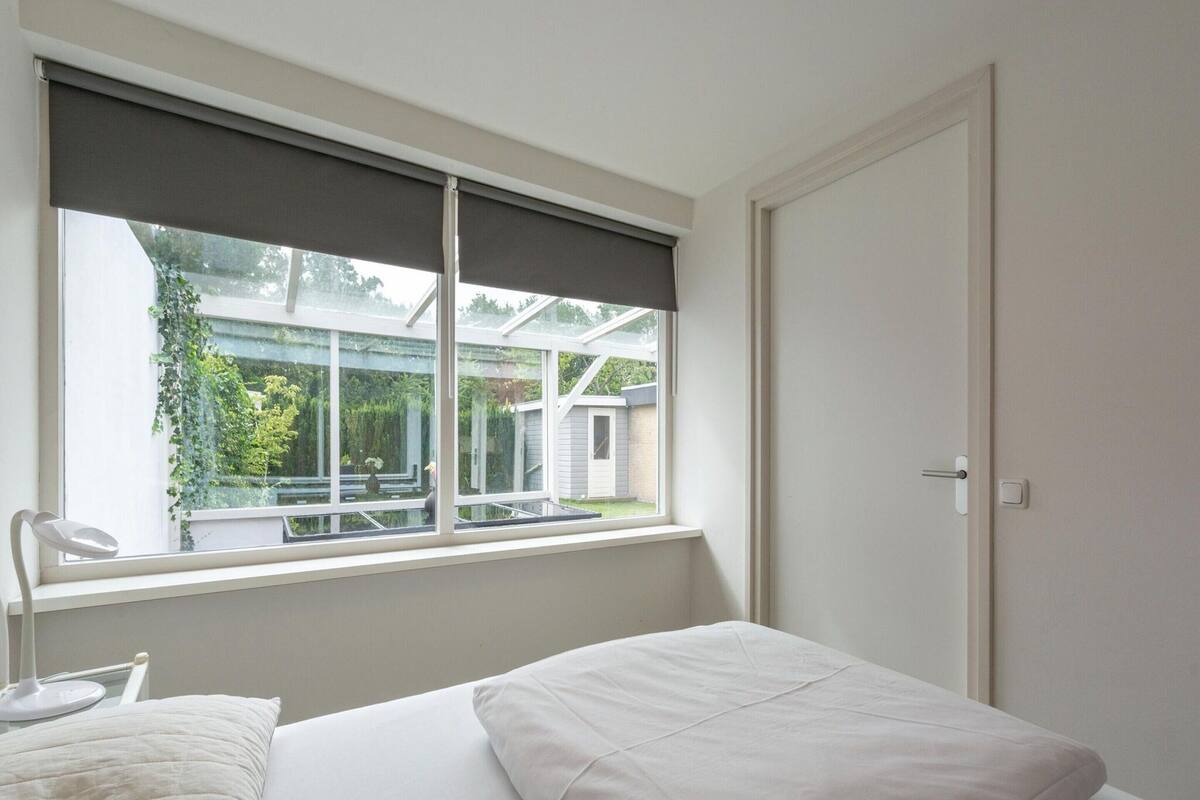 A bedroom with a bed, a window with a view of a garden, and a door.
