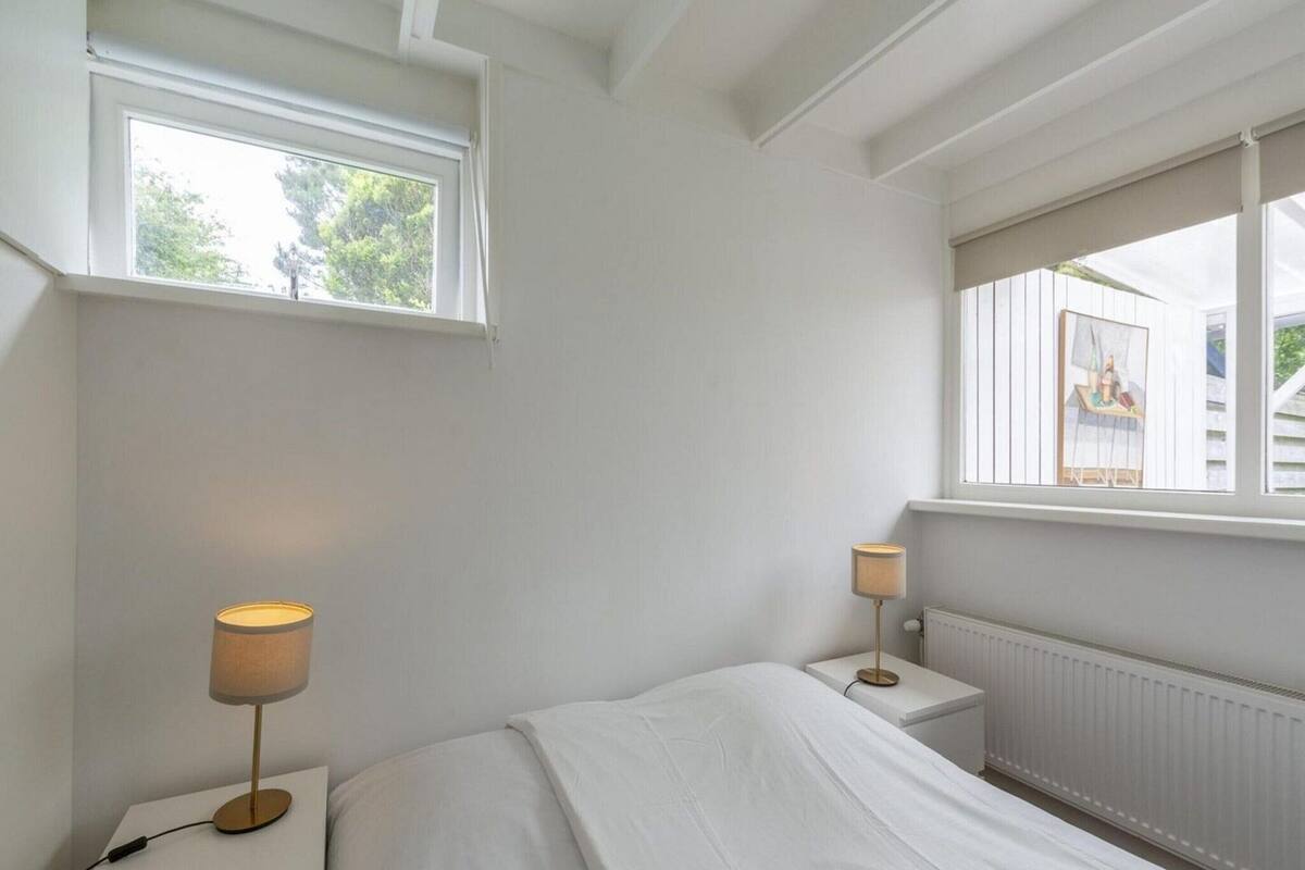 A bedroom with a bed, two bedside tables, a window, and a radiator.