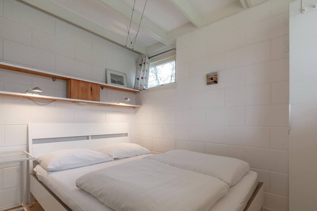 A bedroom with a large bed, wooden headboard, white walls, and a window with a view.