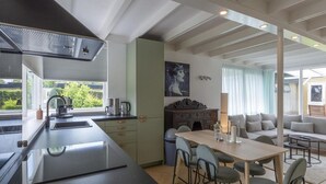 A modern kitchen with a large island, a dining area with a table and chairs, and a living area with a sofa and a lamp. - Comfortable Holiday Home in Sint Maartenszee (Sint Maartensvlotbrug)