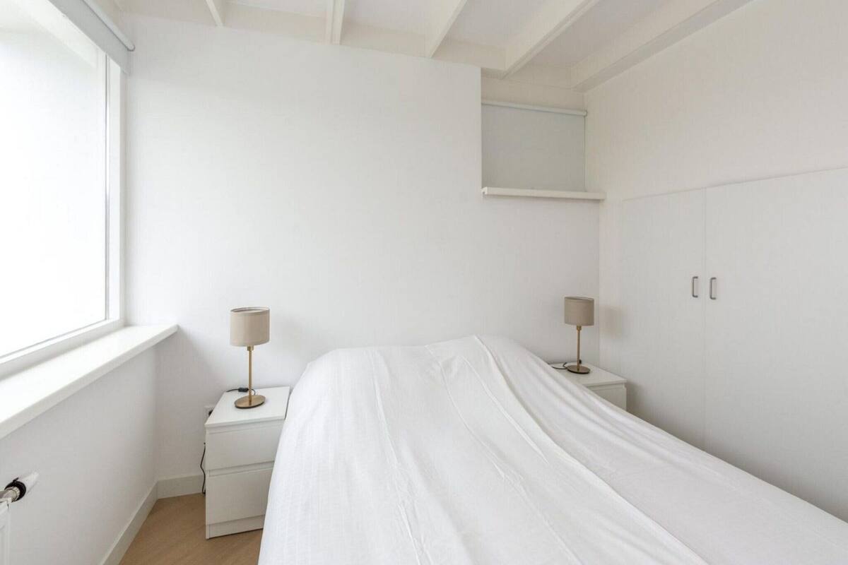 A minimalist bedroom with a bed, bedside lamps, a nightstand, and a wardrobe.