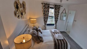 Ett hotellrum med en säng, två sänglampor, ett fönster med gardiner, en spegel och ett element.