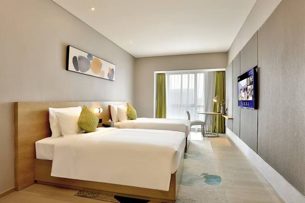 Une chambre d’hôtel avec deux lits, une télévision, un bureau et une fenêtre avec des rideaux.
