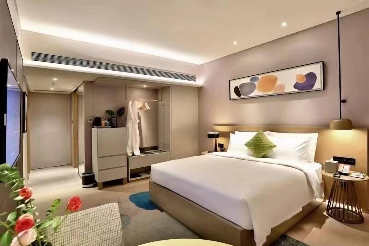 Une chambre d’hôtel moderne dotée d’un grand lit, de tables de chevet, d’une œuvre d’art accrochée au mur et d’une armoire intégrée.