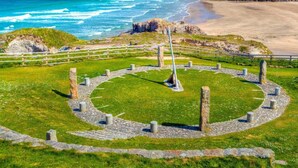 A coastal landscape with a sandy beach, grassy areas, and a rocky outcrop.