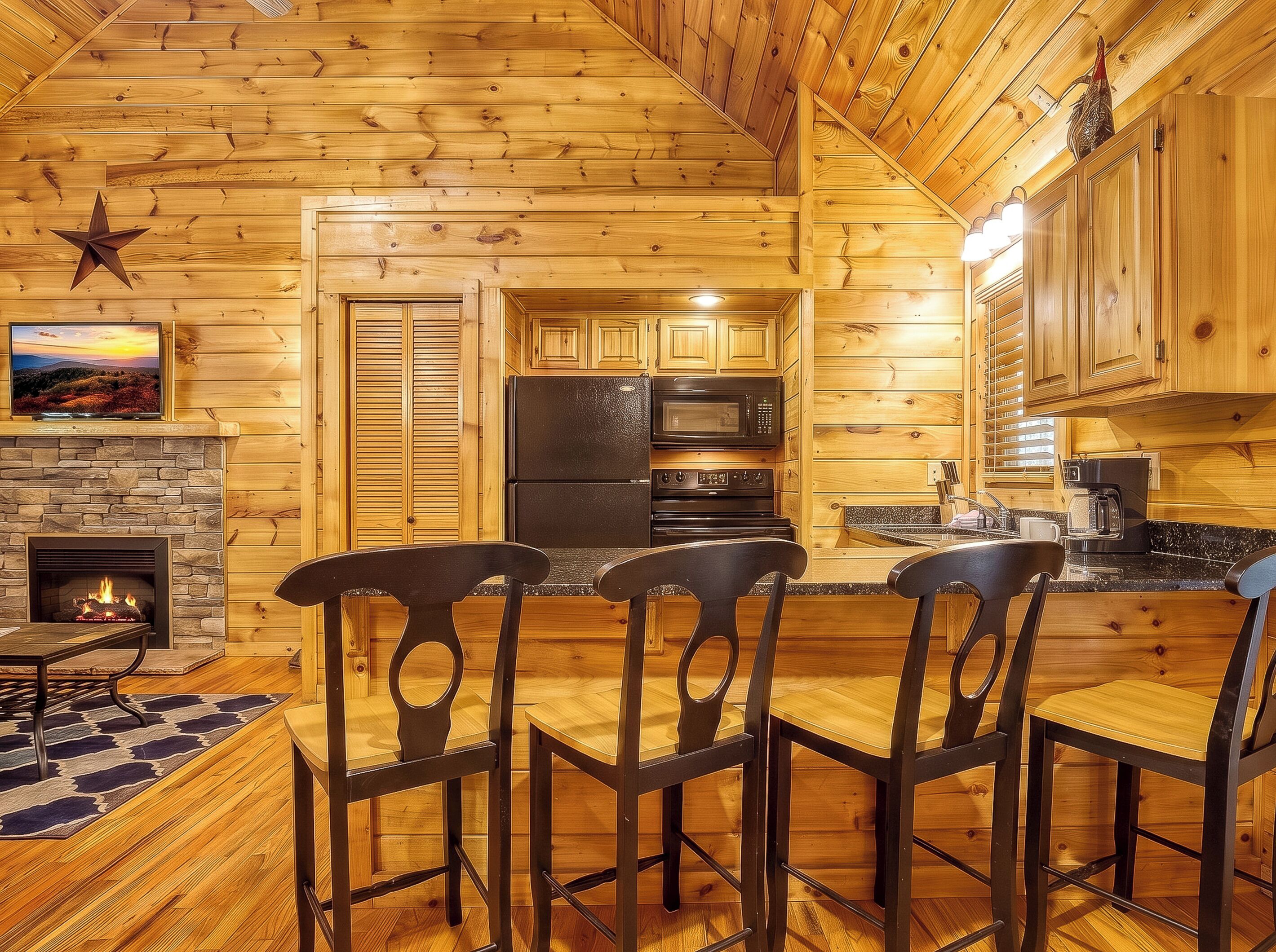 A wooden interior with a stone fireplace, a dining area with chairs, and a kitchen with appliances.