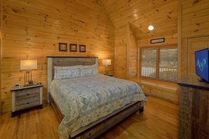 A wooden cabin bedroom with a bed, two bedside tables with lamps, a TV, and a window with blinds. - New Listing! 2 Minutes from Pigeon Forge Parkway! Hot tub/Pool table/Romantic! (Pigeon Forge)