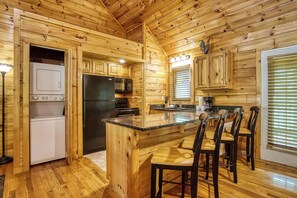 Cocina de cabaña de madera con una isla central, electrodomésticos integrados y un comedor con sillas.