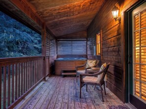 A wooden deck with a hot tub, wicker chairs, and a view of trees.