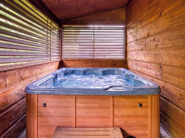 Una cabaña de madera con hidromasaje, paredes de madera y una ventana con persianas.