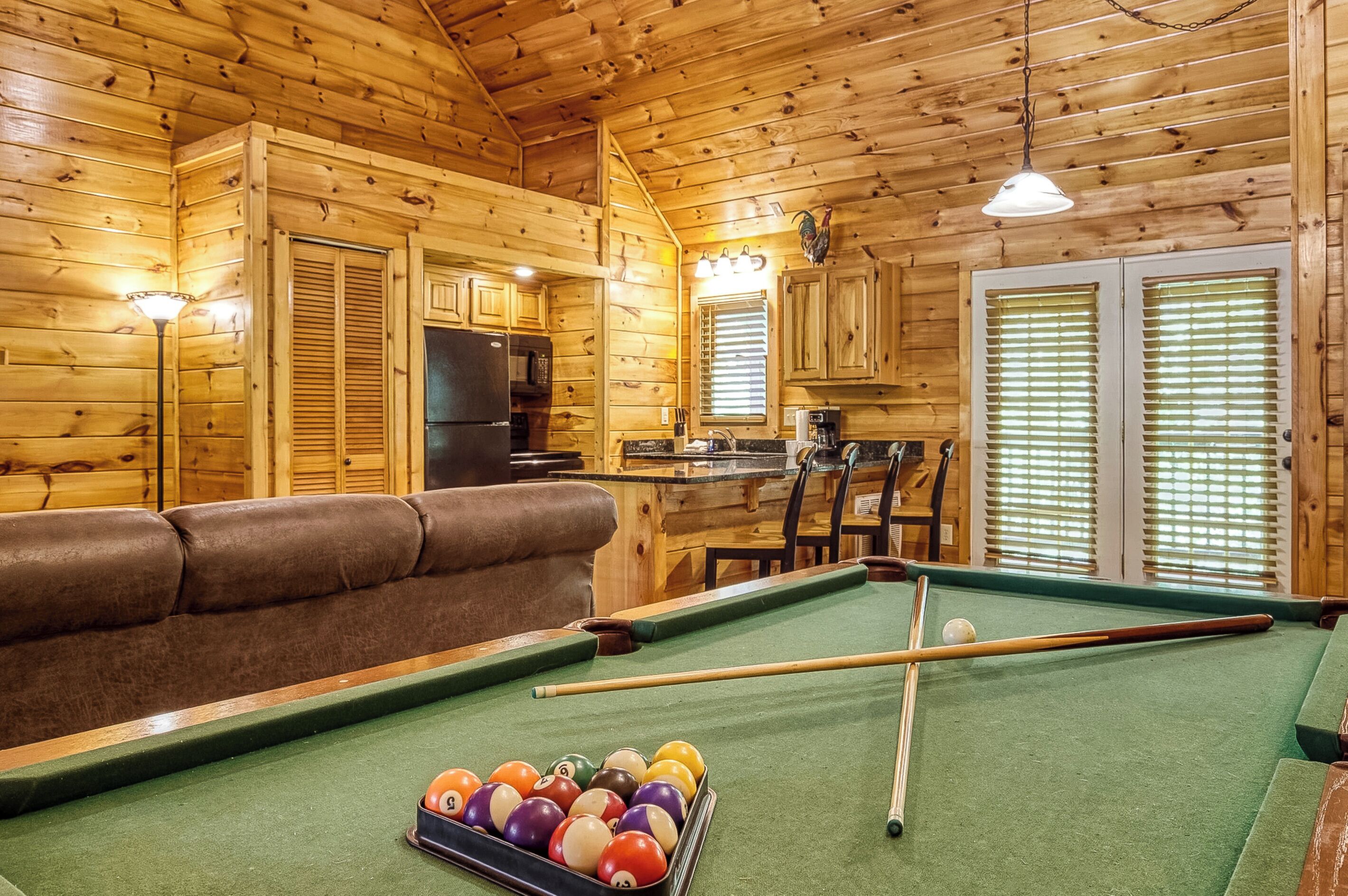 A wooden interior with a pool table, a sofa, and a kitchen area.