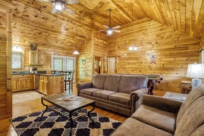 Interior de una cabaña de madera con comedor, cocina y sala de estar con sofá y sillones.