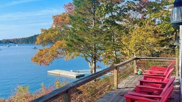 A wooden deck with red Adirondack chairs overlooking a body of water with boats.