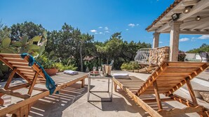 A patio with wooden loungers, a stone table, and a pergola.
