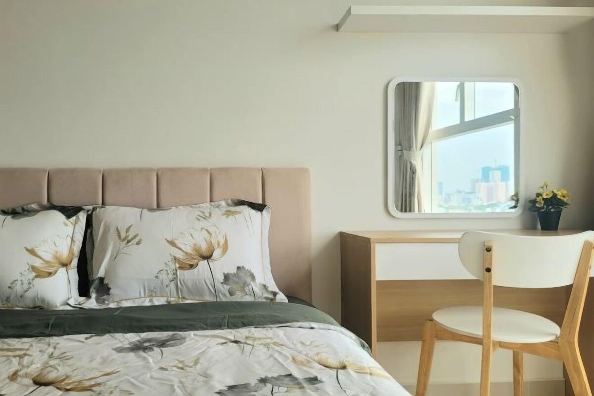 Quarto com cama, cadeira, escrivaninha e janela com vista para edifícios.
