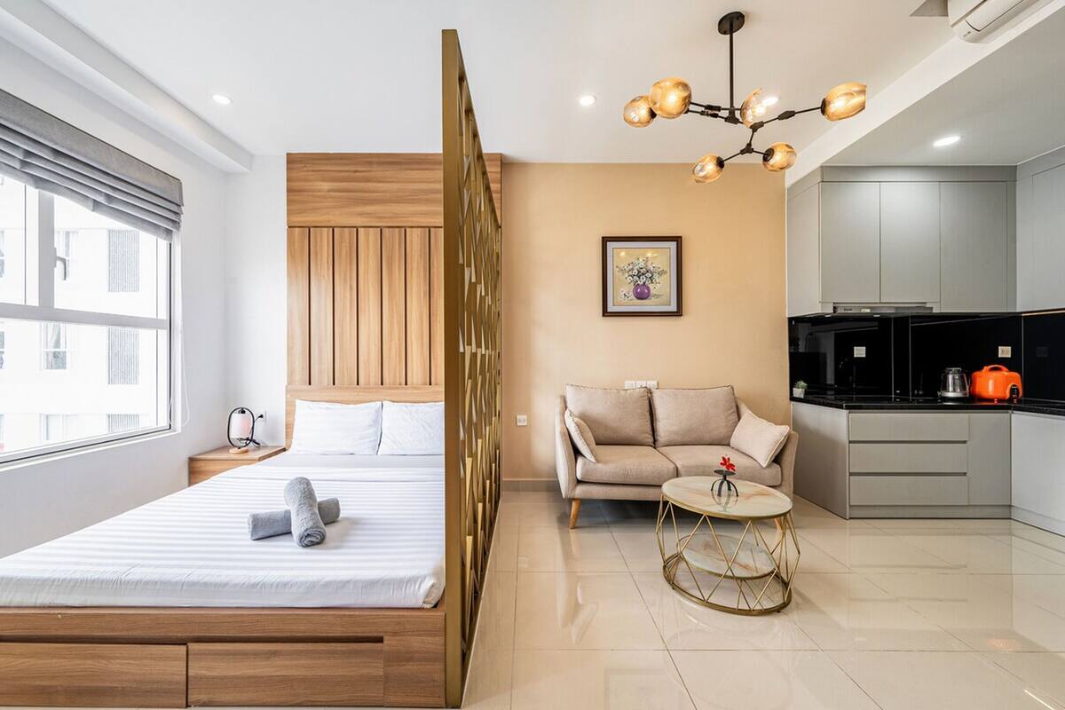 Una habitación de hotel moderna con cama, sofá, una mesita redonda, zona de cocina y un ventanal grande.