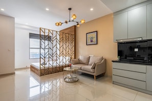 A modern living room with a sofa, a glass coffee table, a decorative partition, and a kitchen area with cabinets.