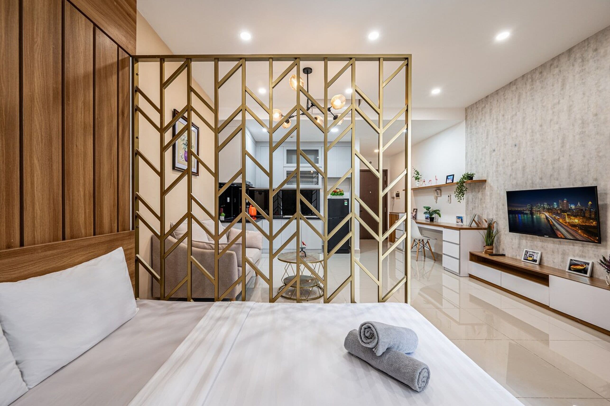 Quarto de hotel com uma cama, vista para a cozinha, televisão e um painel decorativo.