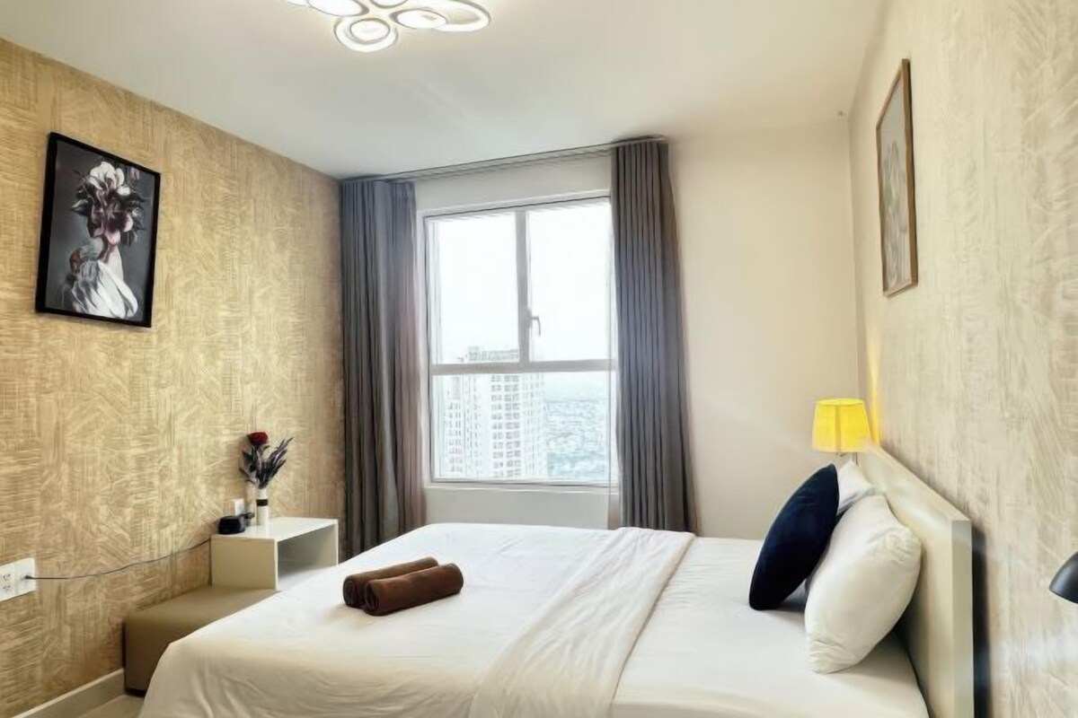Quarto de hotel com cama, janela com cortinas, abajur e quadro na parede.