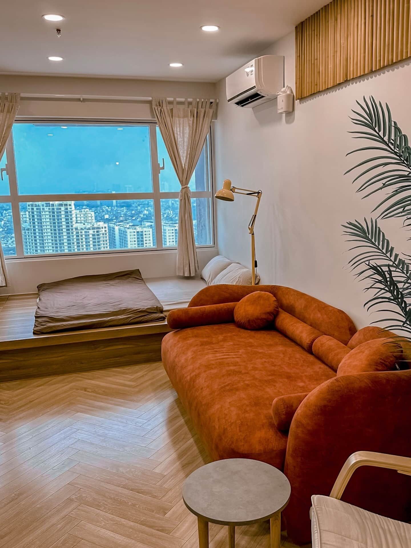 A modern living room with a large window, a sofa, a small table, and a bed.