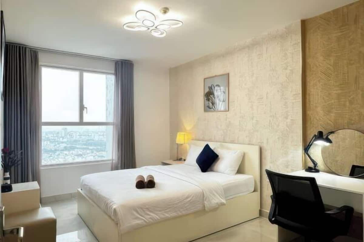 Habitación de hotel con cama, escritorio, silla, lámpara, ventana con cortinas y vistas a la ciudad.