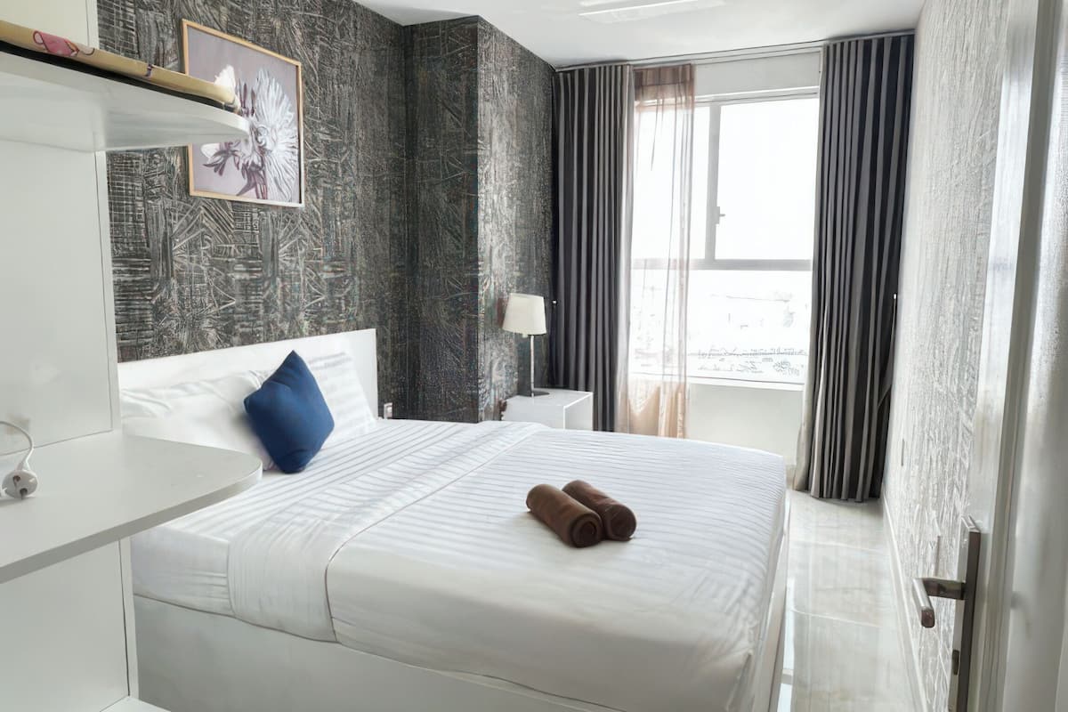Una habitación de hotel con una cama grande, una mesita de noche, una lámpara y una ventana con cortinas.