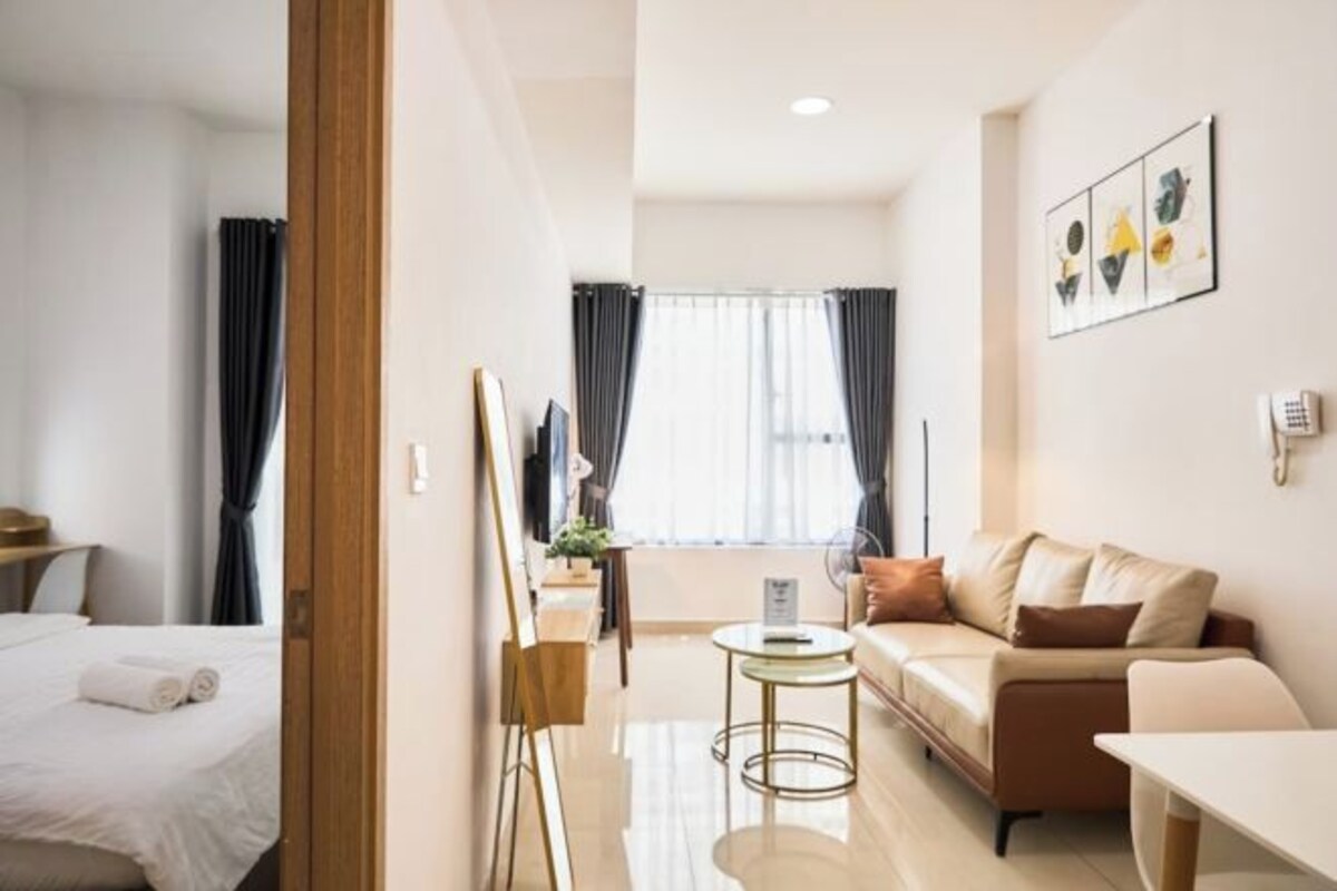 Quarto de hotel com cama, sofá, mesa pequena, pintura e janela com cortinas.