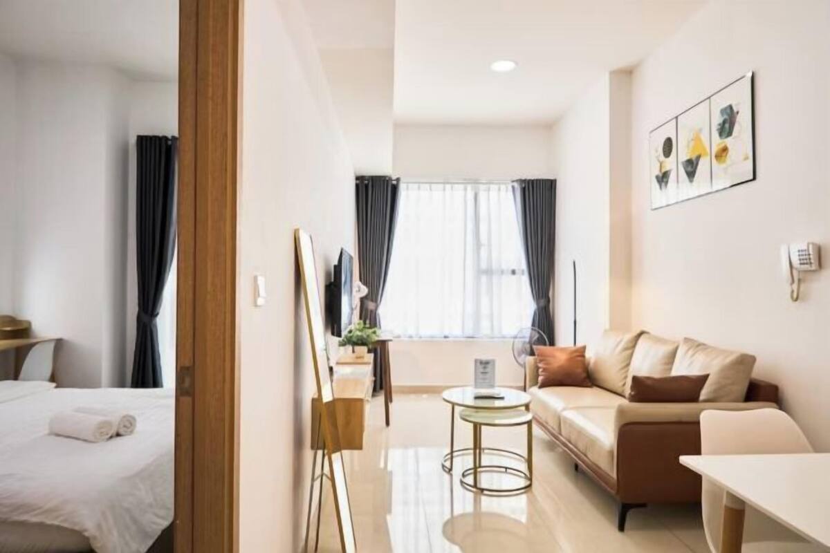 Habitación de hotel con cama, sofá, una mesita, un cuadro y una ventana con cortinas.