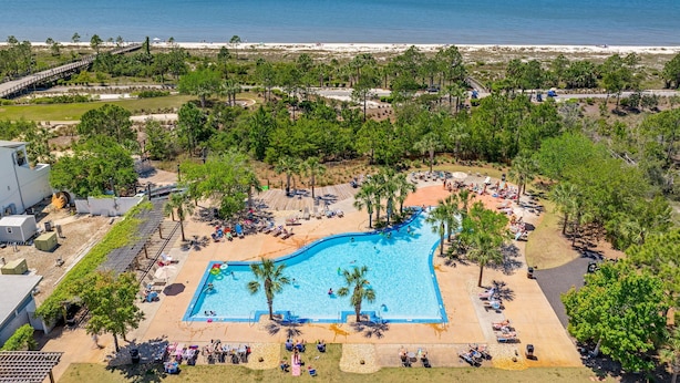 Een resort met een zwembad, omringd door palmbomen en uitzicht op het strand.