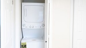 Une buanderie équipée d’un lave-linge et d’un sèche-linge superposés, d’une porte et d’un mur blanc.