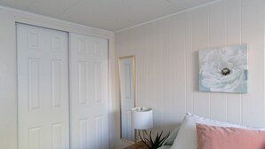 Une chambre à coucher comprenant un lit, une table de chevet, une lampe, un miroir et un mur orné d’un tableau.