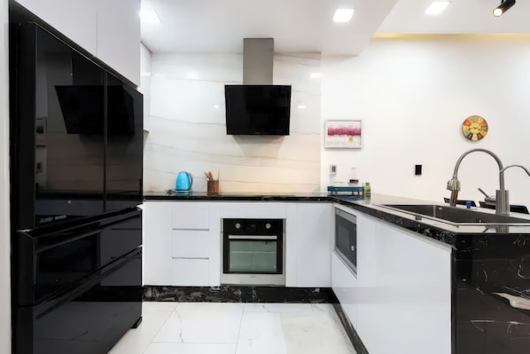Uma cozinha moderna com armários brancos, bancadas pretas, forno embutido e coifa de aço inoxidável.