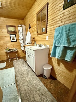A wooden cabin bathroom with a sink, mirror, towel rack, and a small trash bin.