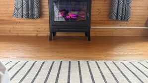 A wood-paneled room with a black wood-burning stove, a striped rug, and patterned curtains. - Little Creek Cabin: Cozy, Adventure-Ready & Dog-Friendly (Anchorage)