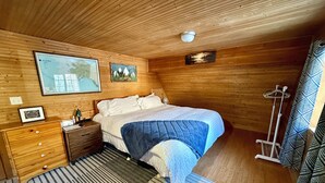 A wooden cabin bedroom with a bed, nightstands, a map, and a coat rack. - Little Creek Cabin: Cozy, Adventure-Ready & Dog-Friendly (Anchorage)