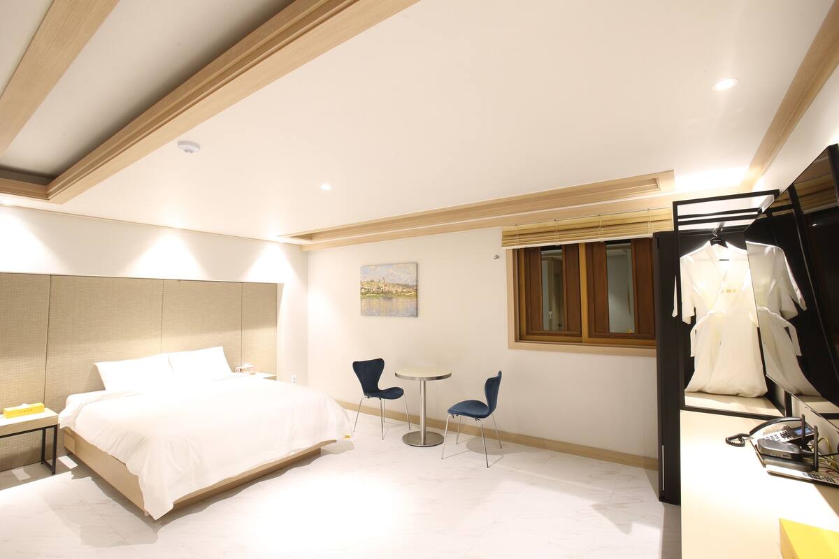Ein modernes Hotelzimmer mit einem großen Bett, zwei Stühlen, einem kleinen Tisch und einem Kleiderschrank.
