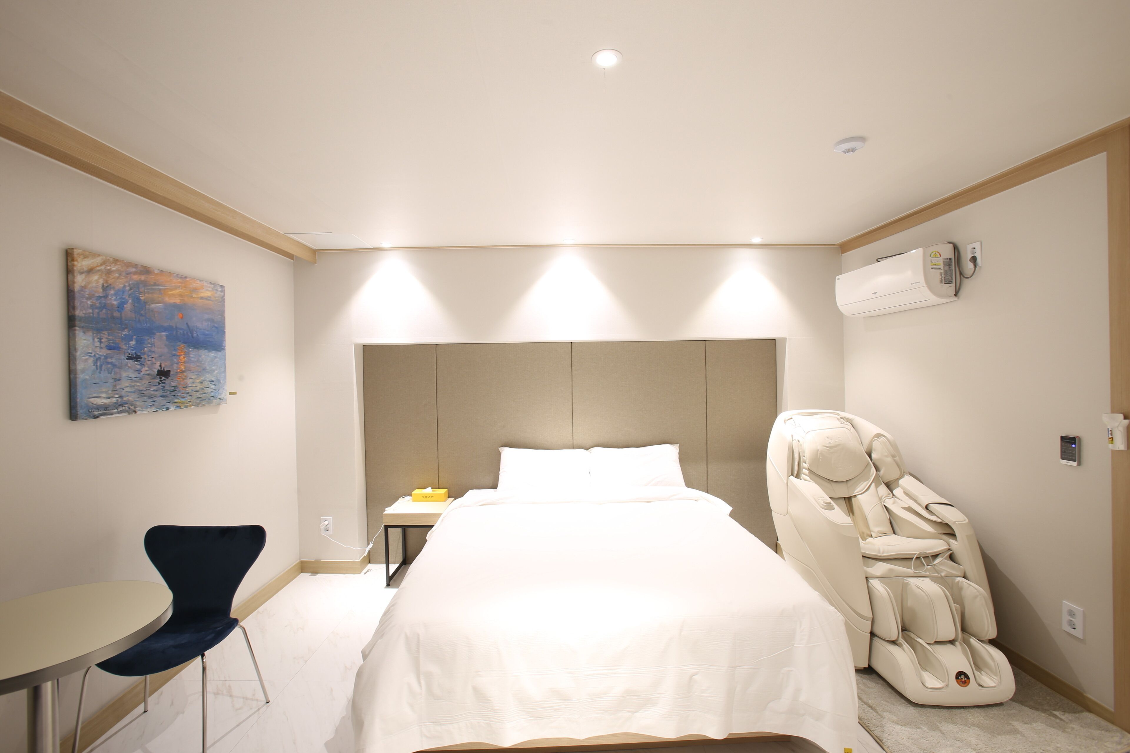 Ett hotellrum med en säng, massagestol, skrivbord, stol och konstverk på väggen.